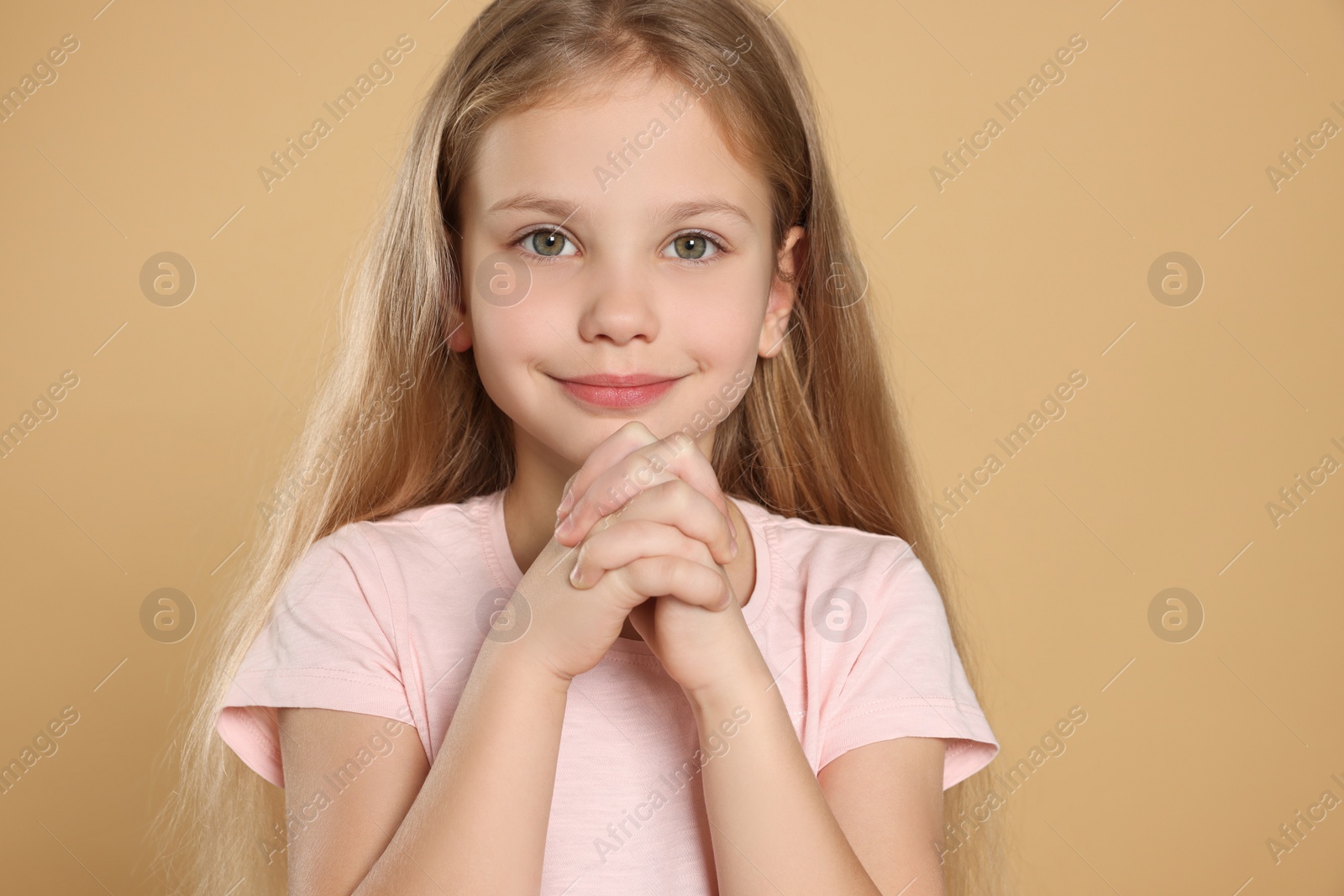 Photo of Girl with clasped hands praying on beige background