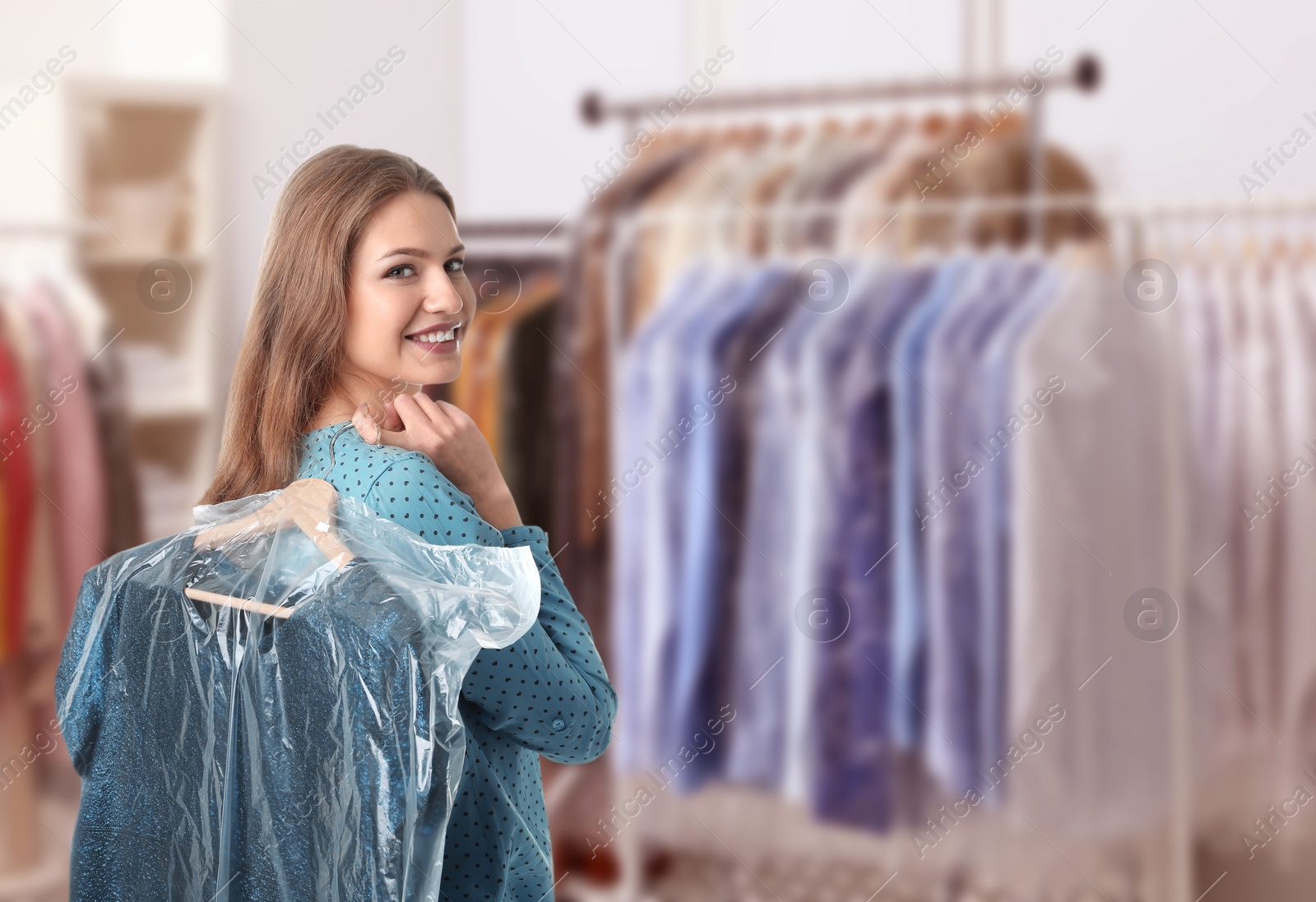 Image of Dry-cleaning service. Happy woman holding hanger with dress in plastic bag indoors, space for text