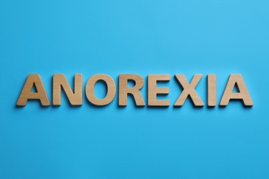 Photo of Word Anorexia made of wooden letters on light blue background, flat lay