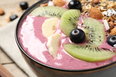 Photo of Delicious acai smoothie with granola and fruits on table, closeup