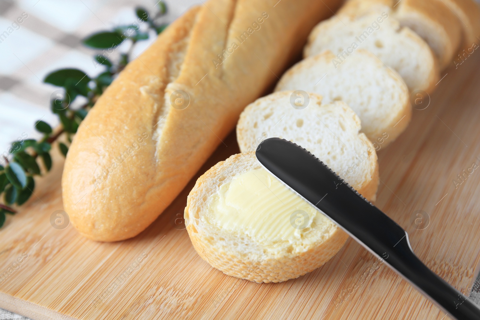 Photo of Whole and cut baguettes with fresh butter on wooden board, closeup