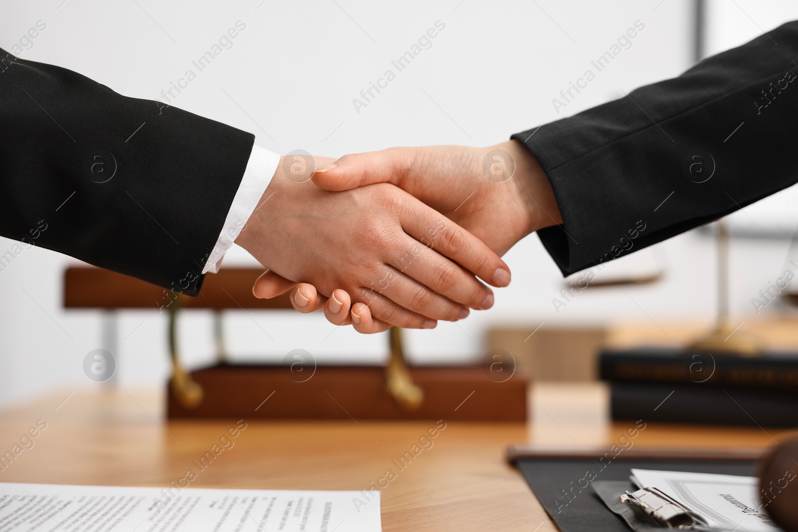 Photo of Notary shaking hands with client at wooden table in office, closeup