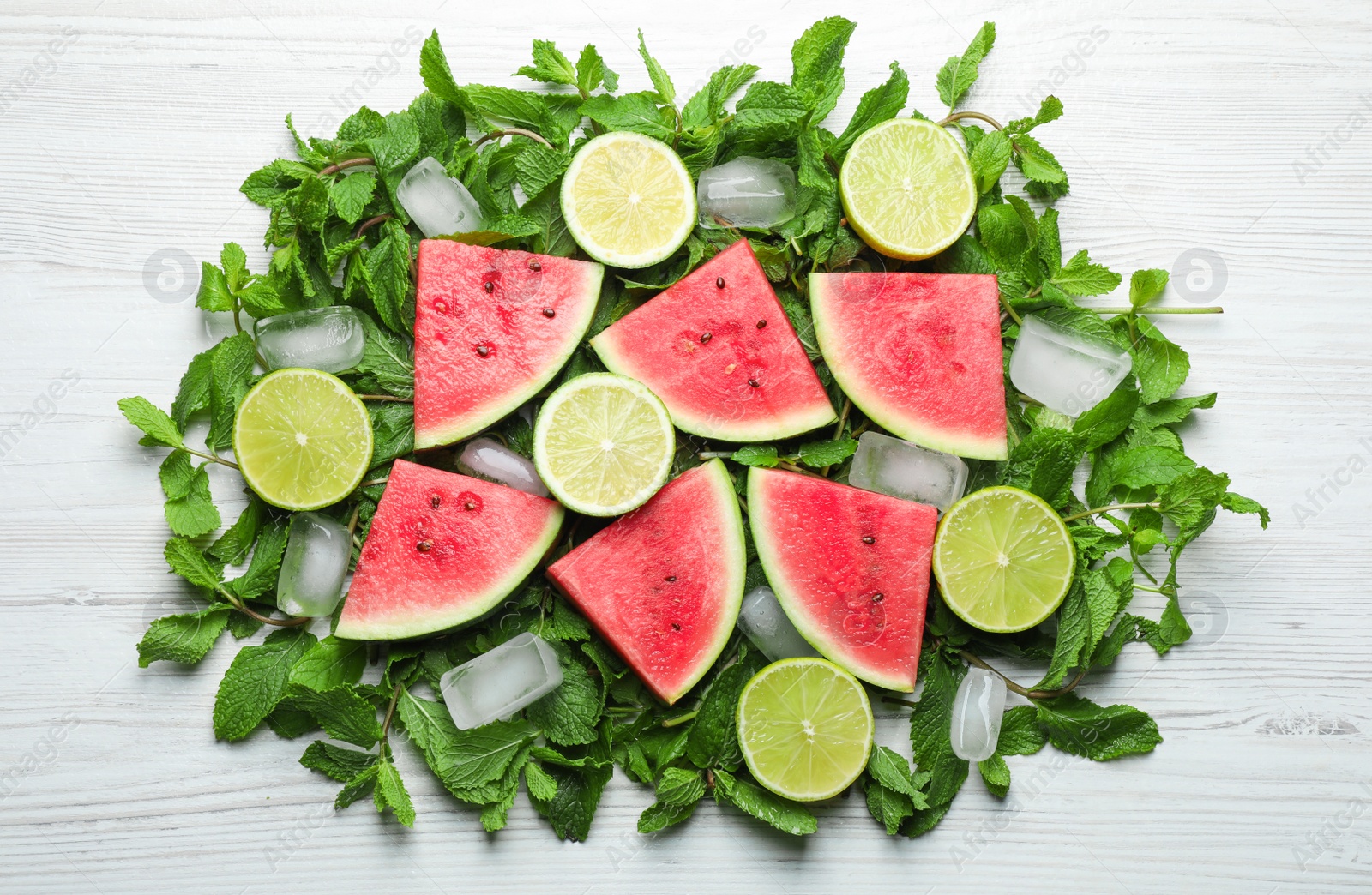 Photo of Tasty sliced watermelon, limes, mint and ice on white wooden table, flat lay