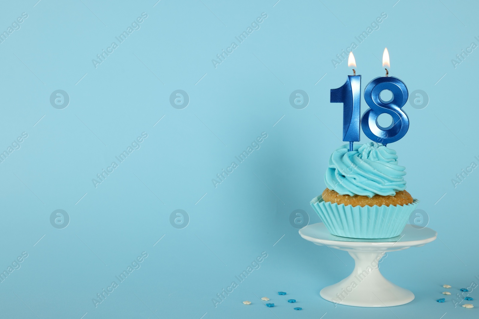 Photo of Delicious cupcake with number shaped candles on light blue background, space for text. Coming of age party - 18th birthday