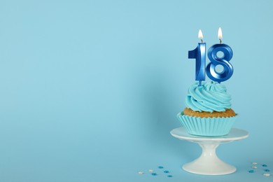 Photo of Delicious cupcake with number shaped candles on light blue background, space for text. Coming of age party - 18th birthday