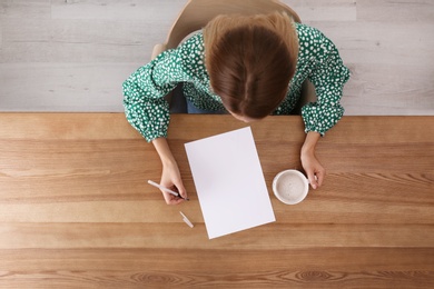 Woman writing on sheet of paper at table indoors, top view