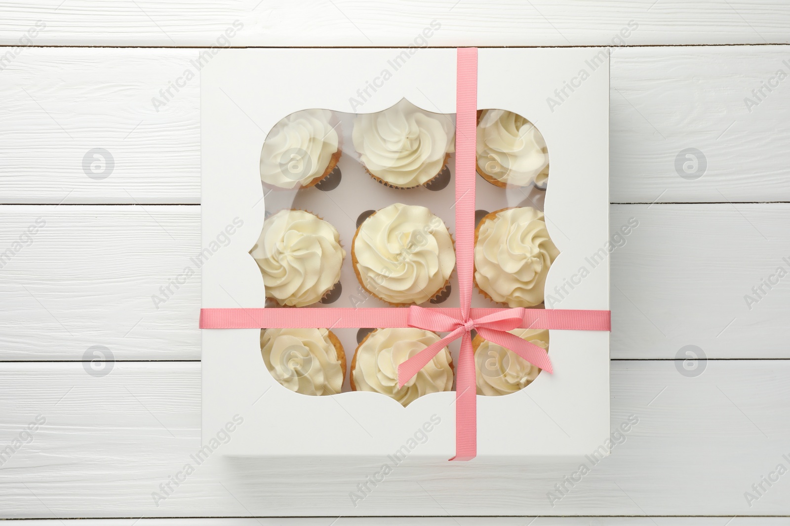 Photo of Tasty cupcakes with vanilla cream in box on white wooden table, top view