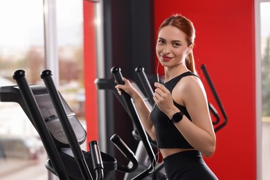 Photo of Athletic young woman with earphones doing exercise with air walker in gym