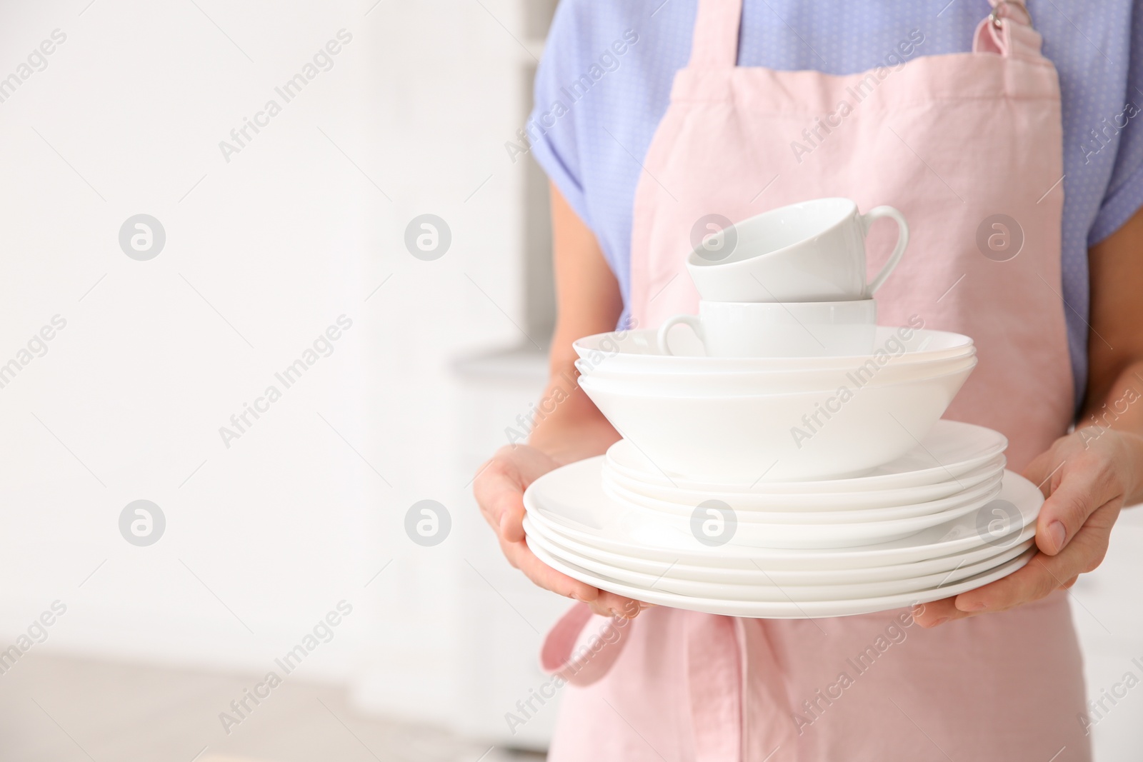 Photo of Woman with clean dishes and cups in kitchen, closeup. Space for text