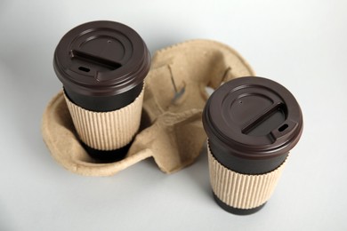 Photo of Takeaway paper coffee cups with sleeves, plastic lids and cardboard holder on grey background
