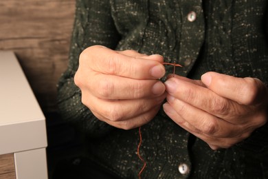 Photo of Closeup view of woman threading needle indoors. Sewing equipment