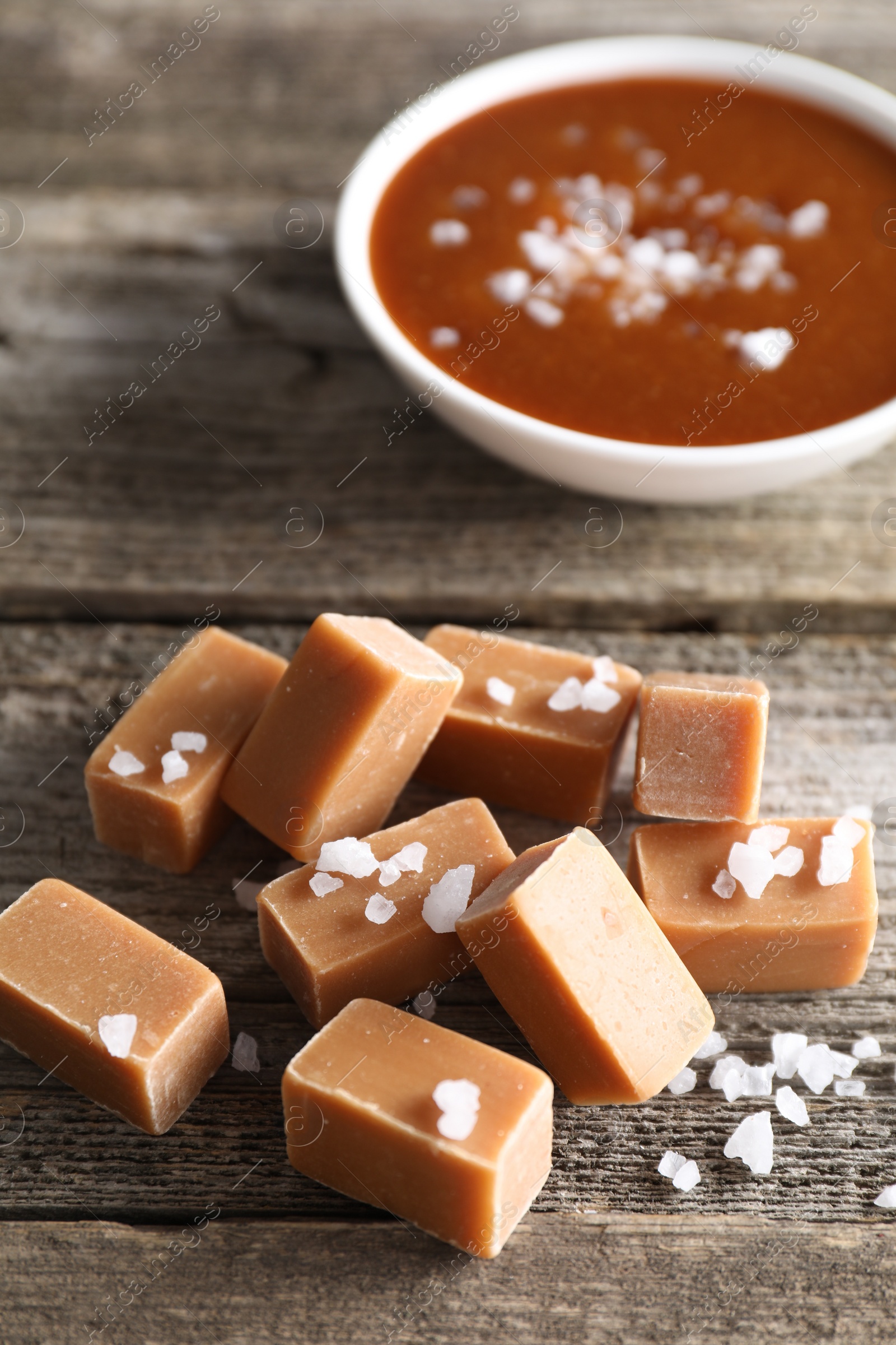 Photo of Yummy caramel candies with sea salt on wooden table, closeup