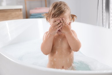 Photo of Playful little girl covering face while taking foamy bath at home