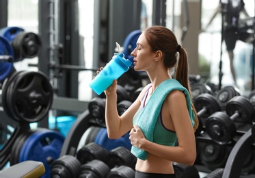 Athletic young woman drinking protein shake in gym