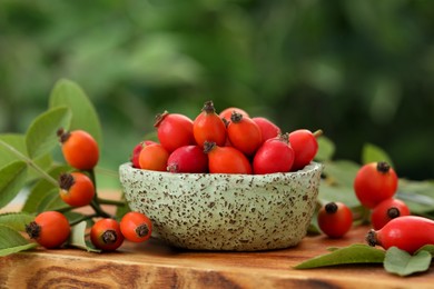 Photo of Ripe rose hip berries with green leaves on wooden table outdoors