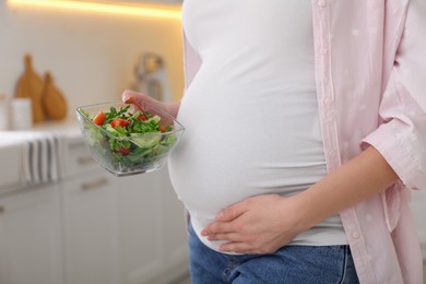 Photo of Young pregnant woman with vegetable salad in kitchen, closeup. Healthy eating