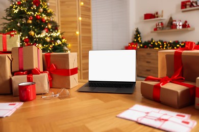 Photo of Christmas time. Laptop with blank screen, gift boxes and letters on table at home