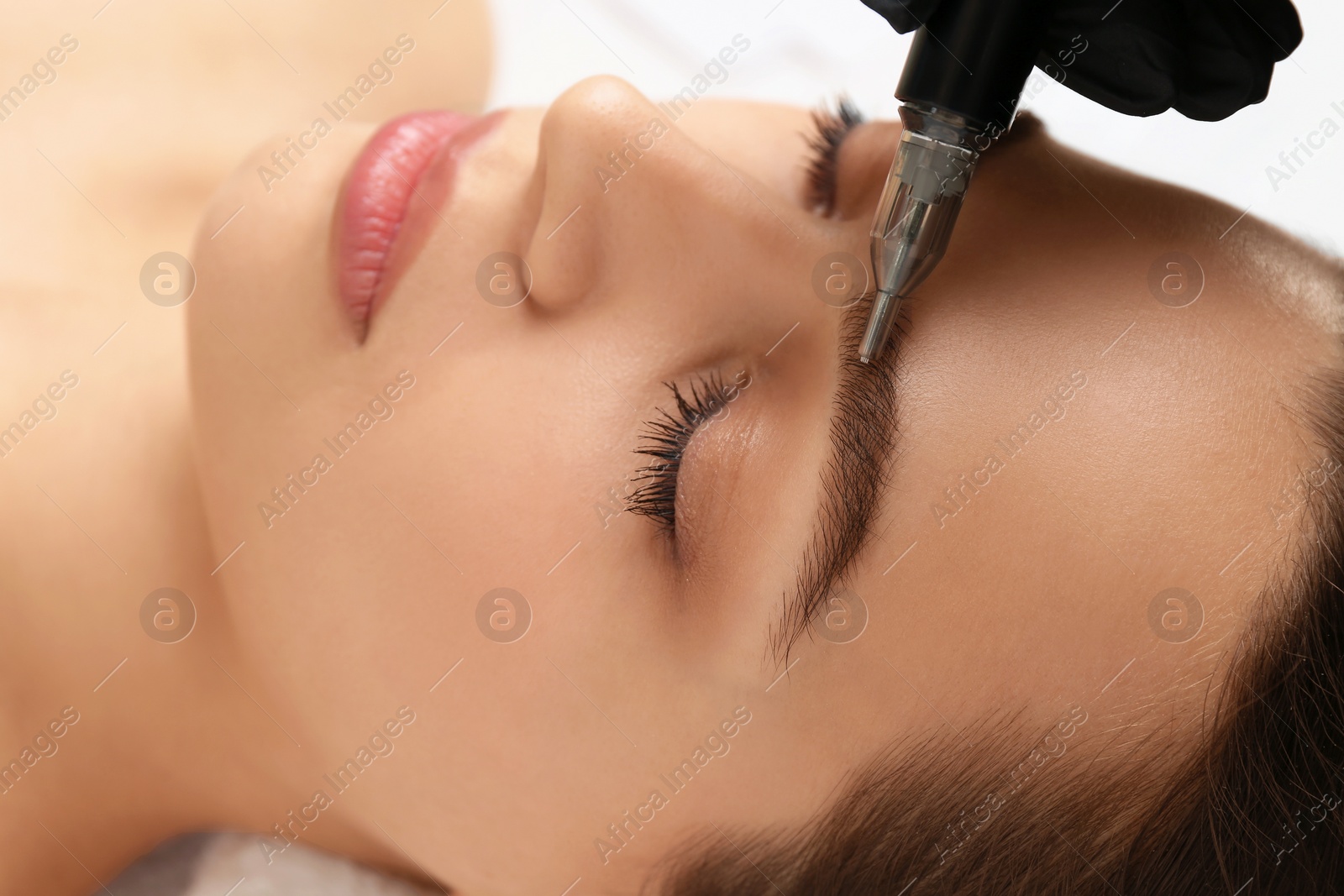 Photo of Beautician making permanent eyebrow makeup to young woman, closeup