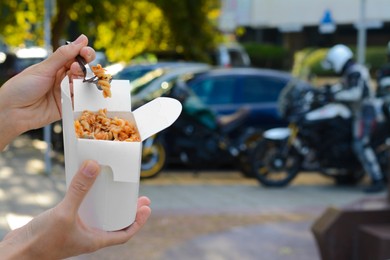 Woman eating takeaway noodles from paper box with fork outdoors, closeup and space for text. Street food