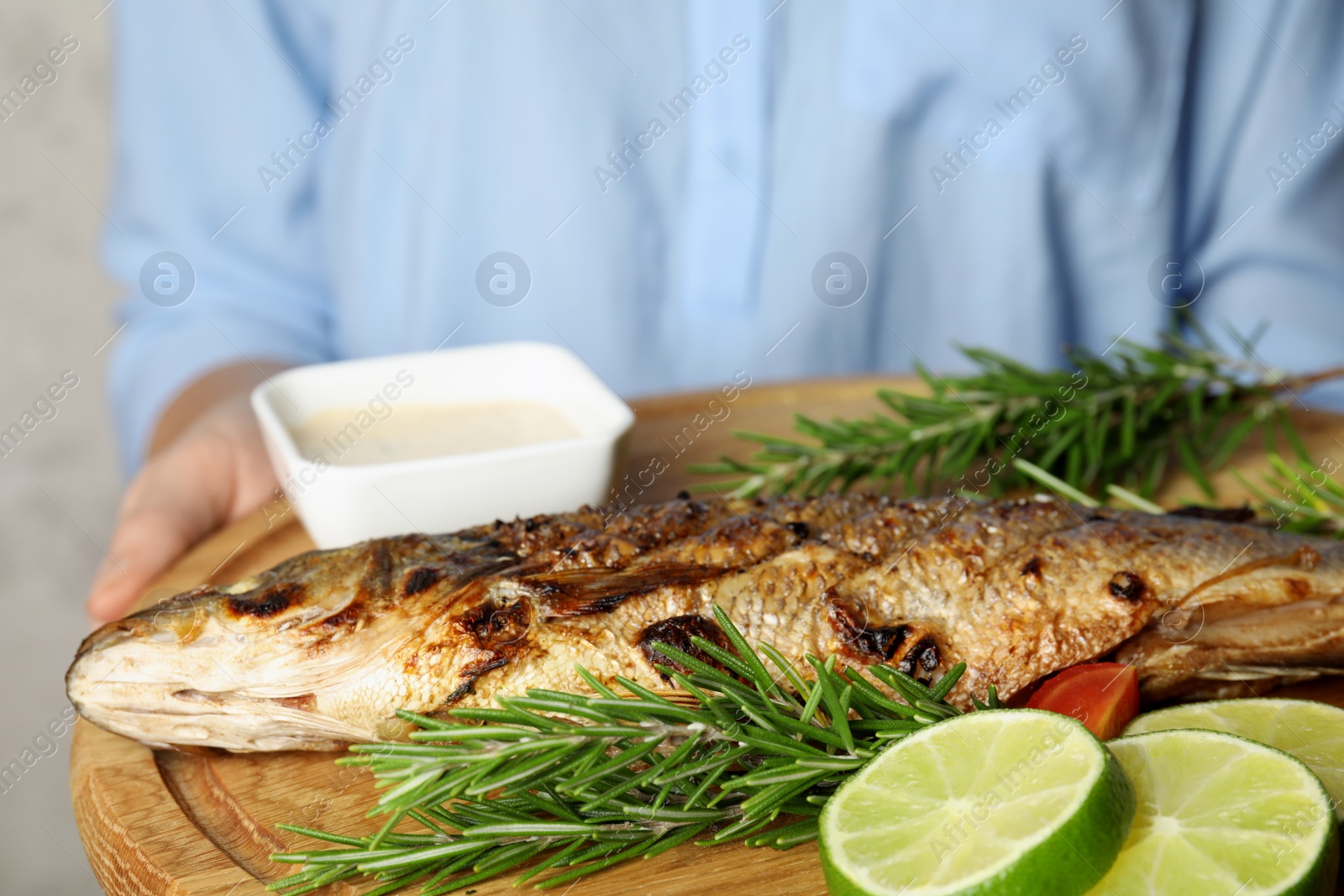 Photo of Woman holding wooden board with delicious grilled fish, closeup