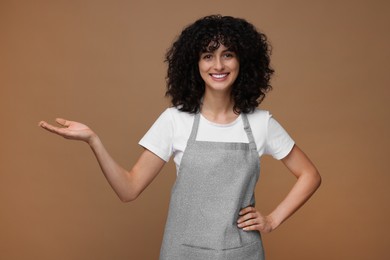 Photo of Happy woman wearing kitchen apron on brown background. Mockup for design