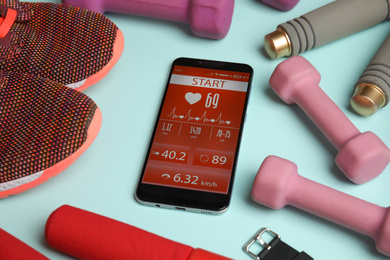 Photo of Smartphone with heart rate monitor app and fitness accessories on light blue background