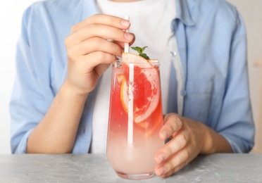 Woman with glass of grapefruit refreshing drink at grey marble table, closeup