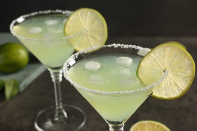 Delicious Margarita cocktail with ice cubes in glasses and lime on grey table, closeup