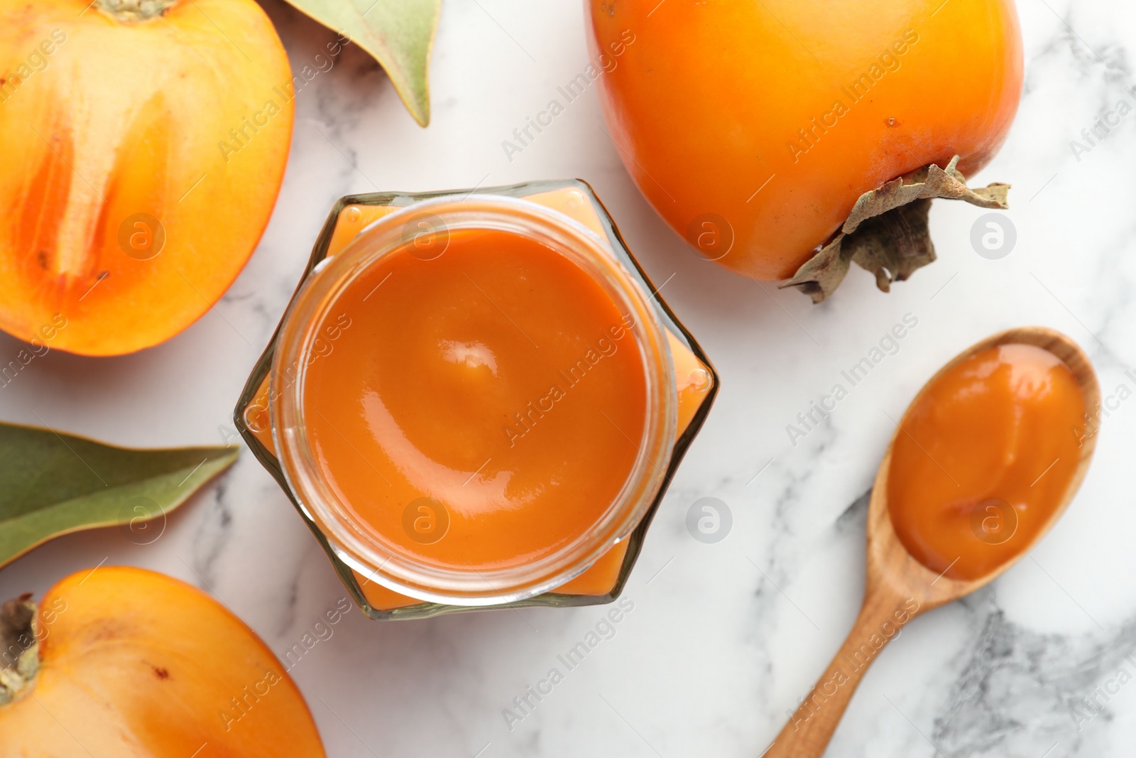 Photo of Delicious persimmon jam and fresh fruits on white marble table, flat lay