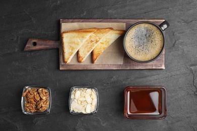 Photo of Tasty breakfast with coffee, toasts, nuts and jam on dark table, flat lay