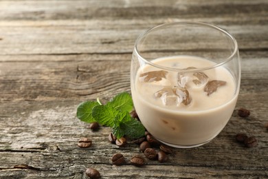 Photo of Coffee cream liqueur in glass, mint and beans on wooden table, closeup