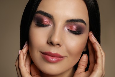 Beautiful young woman with evening makeup on brown background, closeup. Eye shadow product
