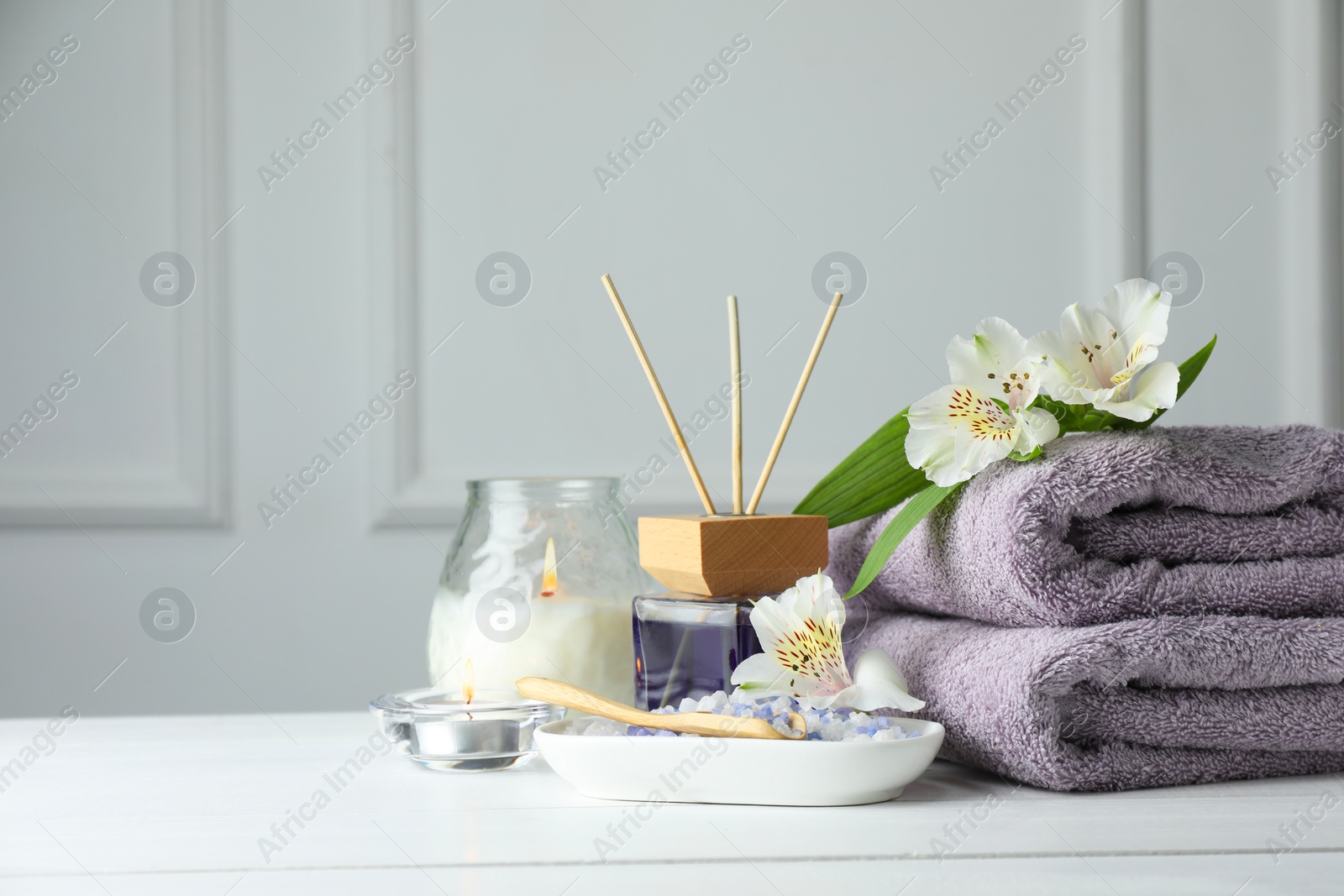 Photo of Spa composition. Towels, burning candles, reed air freshener, sea salt and beautiful flowers on white wooden table, space for text