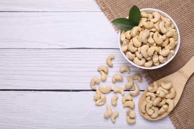 Photo of Tasty cashew nuts and green leaves on white wooden table, flat lay