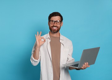 Photo of Handsome man with laptop showing OK gesture on light blue background