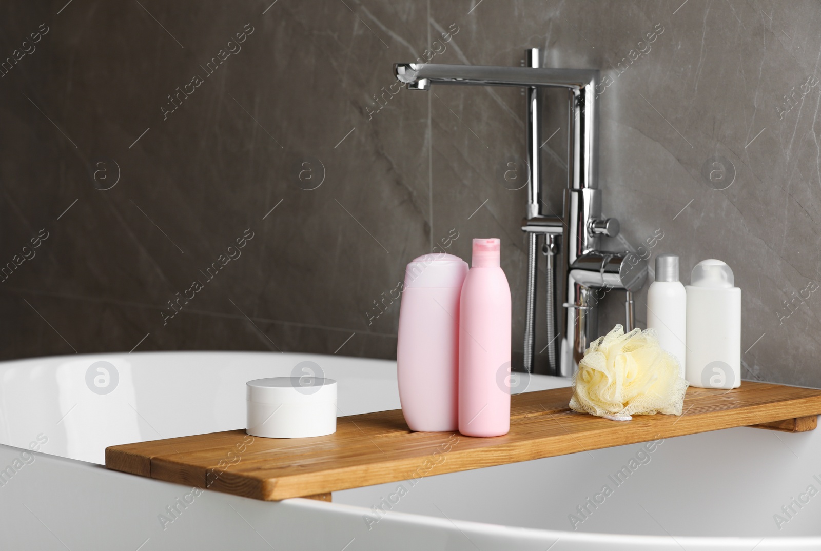 Photo of Wooden bath tray with shampoo, conditioner and other toiletries on tub indoors