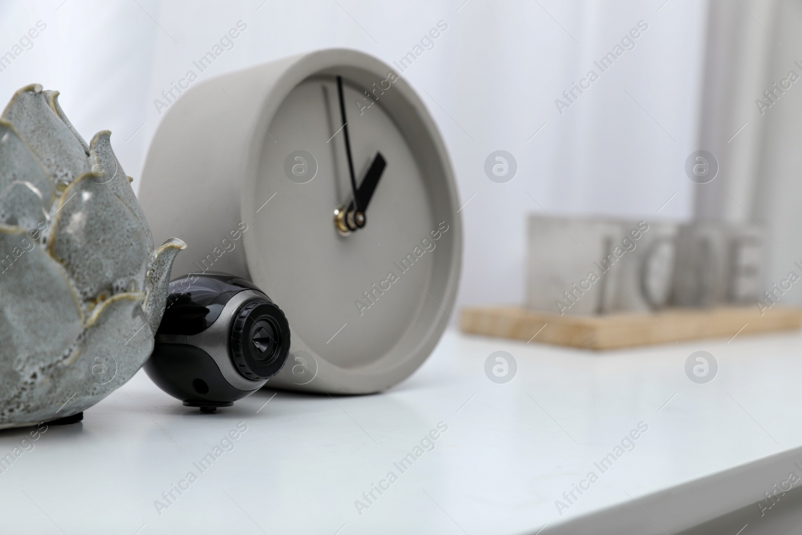 Photo of Small camera hidden near alarm clock on white table indoors