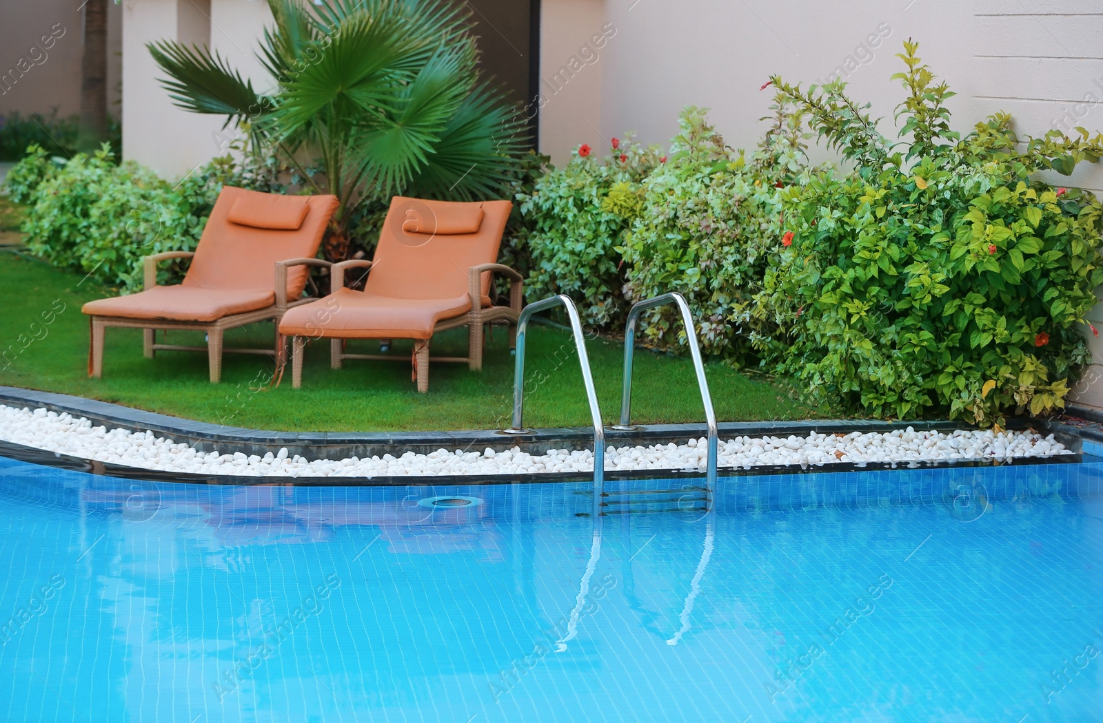 Photo of Sunbeds near modern swimming pool with stairs at resort