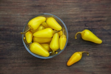 Photo of Glass bowl of pickled yellow jalapeno peppers on wooden table, flat lay