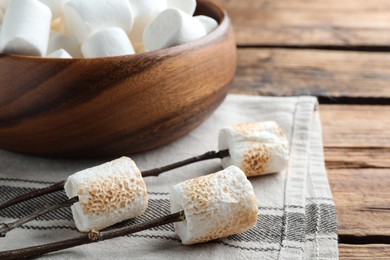 Sticks with roasted marshmallows on wooden table, closeup