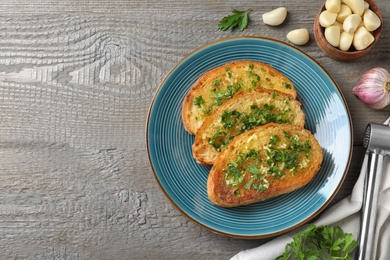 Photo of Slices of toasted bread with garlic and herb on wooden table, flat lay. Space for text