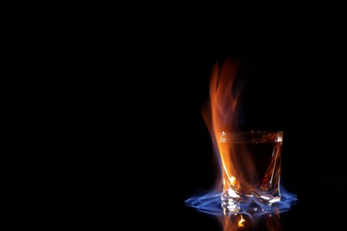 Photo of Glass with flaming vodka on black background, space for text