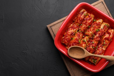 Photo of Delicious stuffed cabbage rolls cooked with homemade tomato sauce on black textured table, top view. Space for text