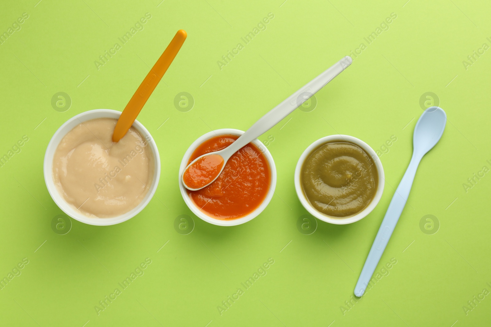Photo of Bowls with healthy baby food and spoons on light green background, flat lay