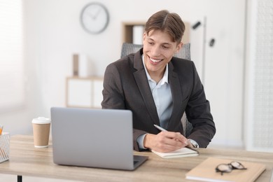 Photo of Man taking notes during webinar at wooden table indoors