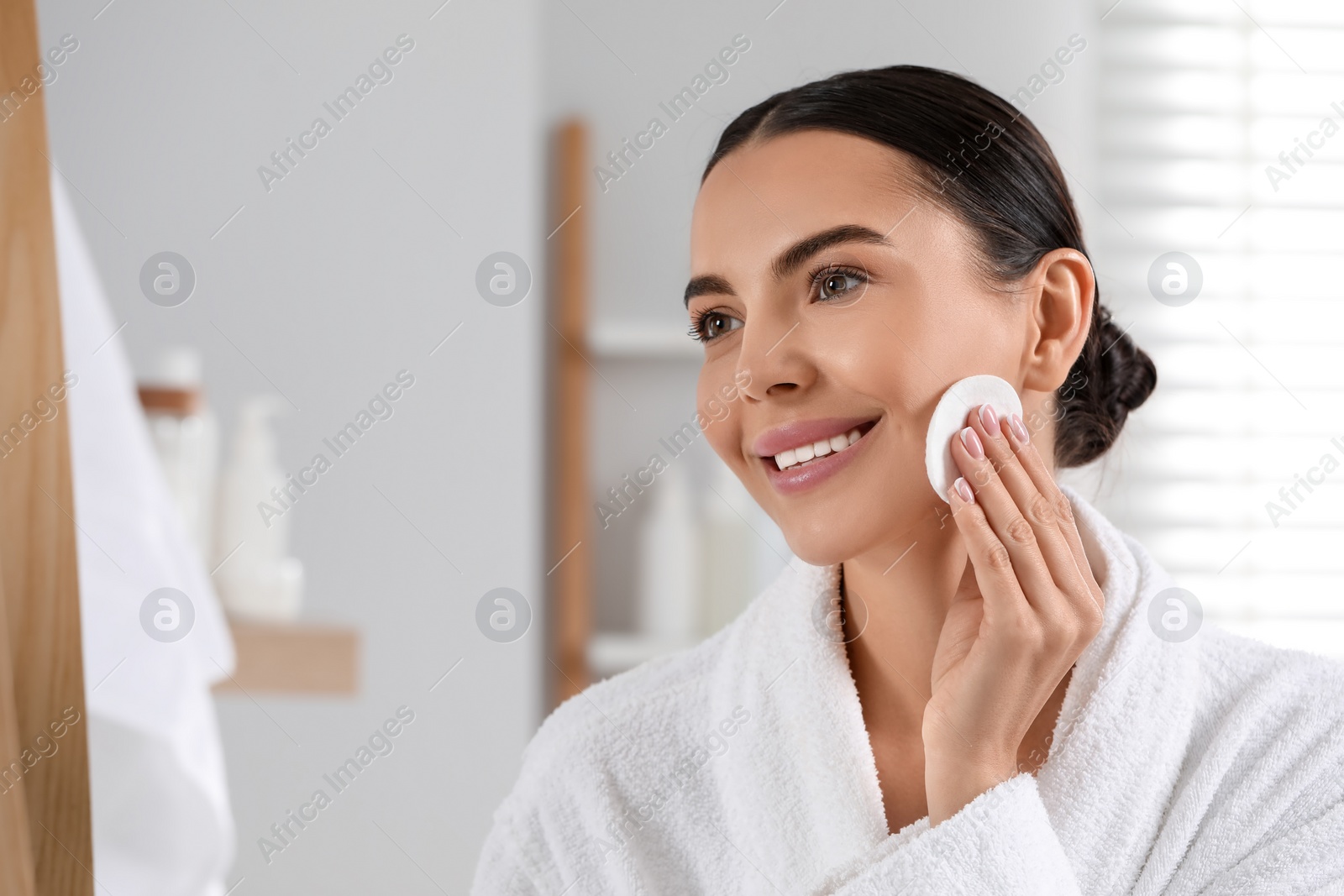 Photo of Beautiful woman removing makeup with cotton pad in bathroom, space for text