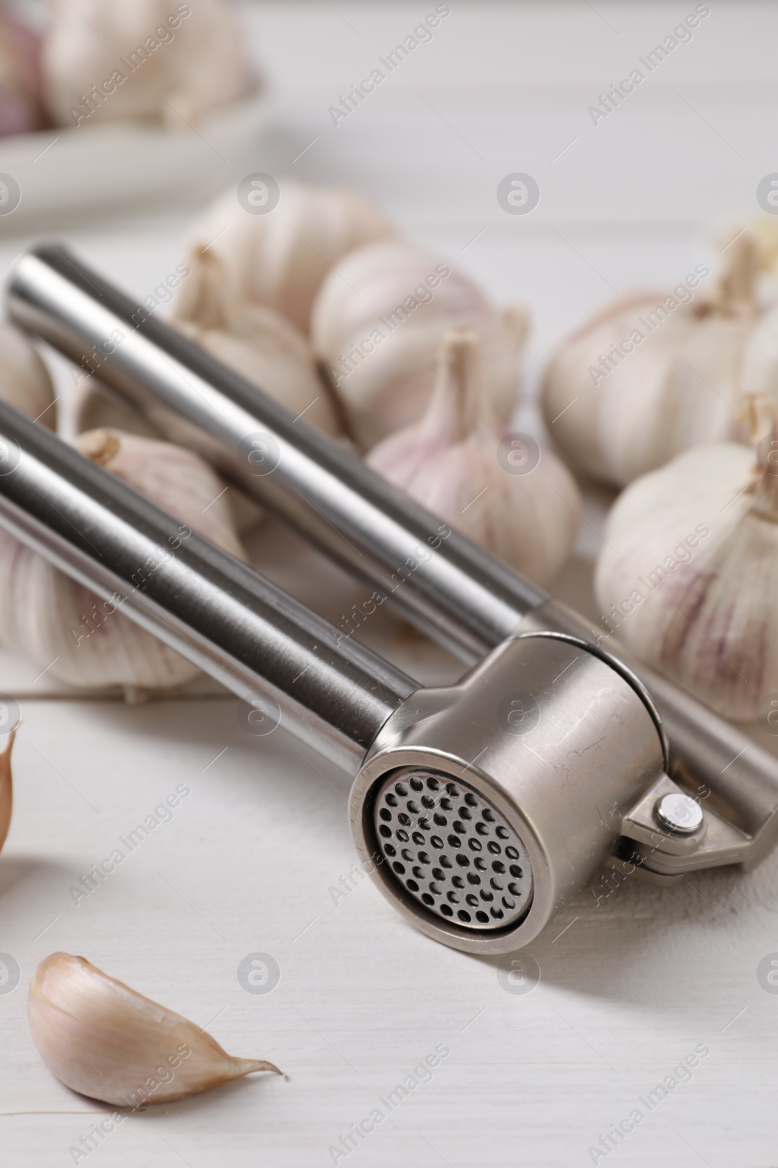 Photo of Metal press and garlic on white wooden table, closeup