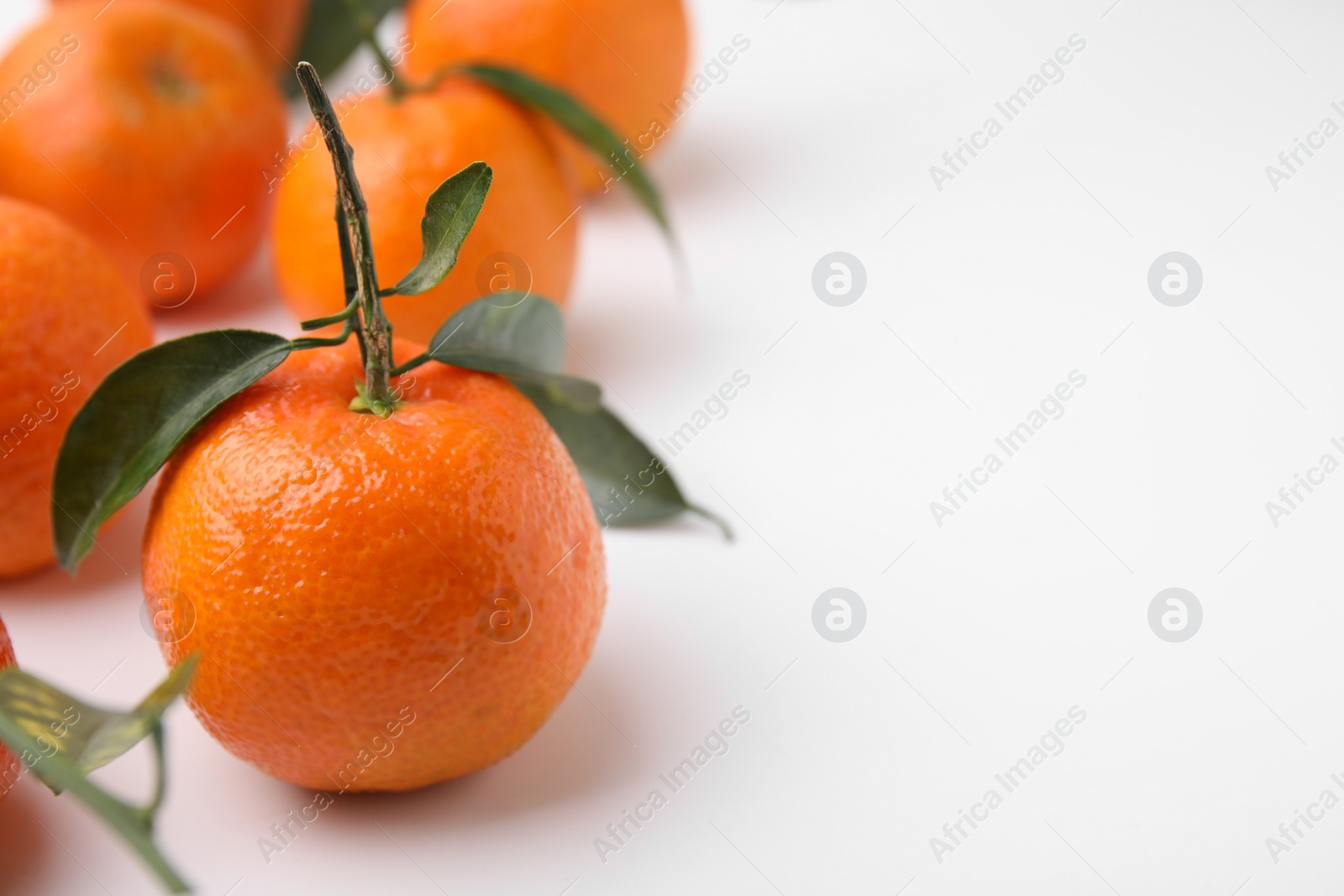 Photo of Fresh ripe tangerines with leaves on white background, closeup. Space for text