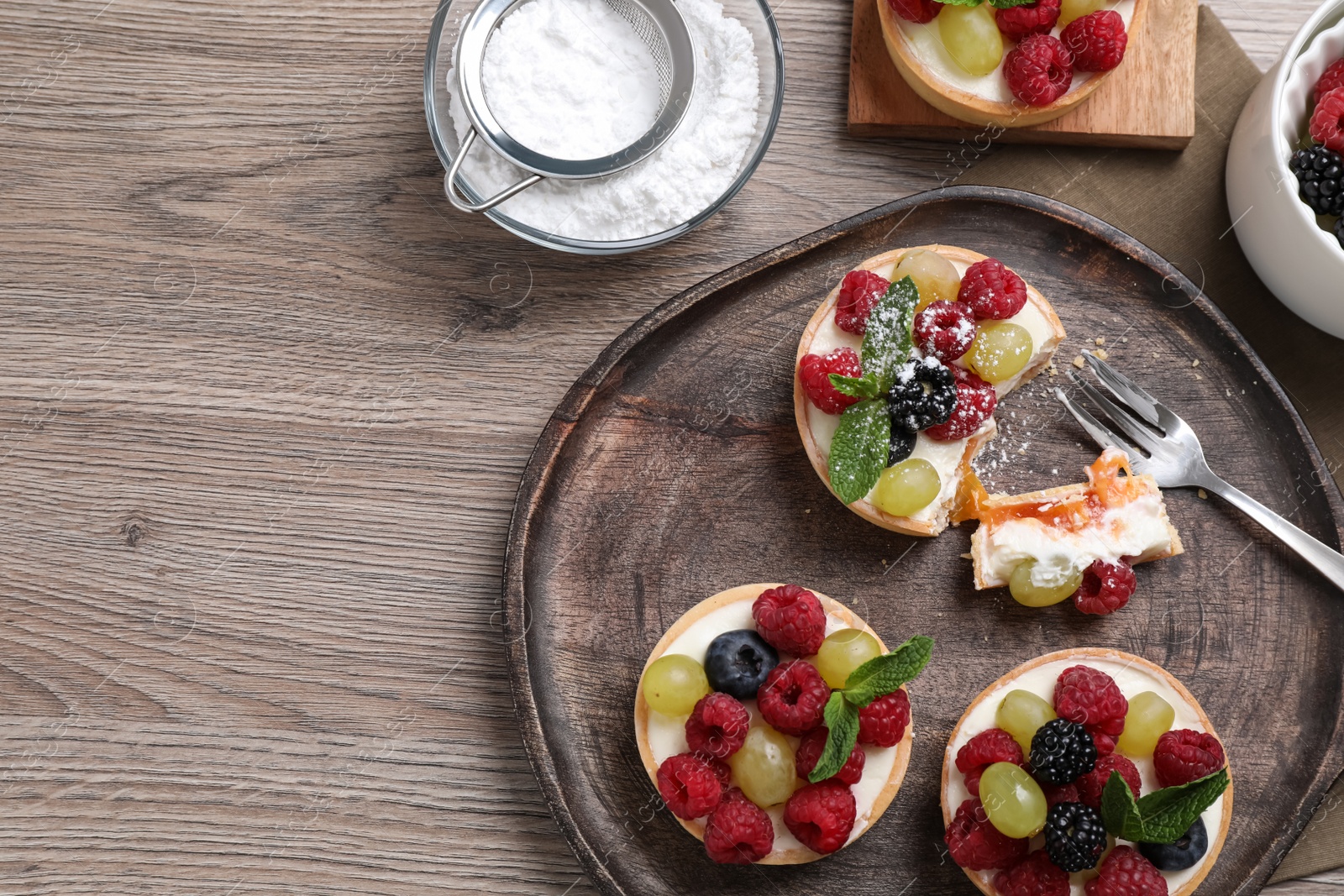 Photo of Delicious tartlets with berries on wooden table, flat lay