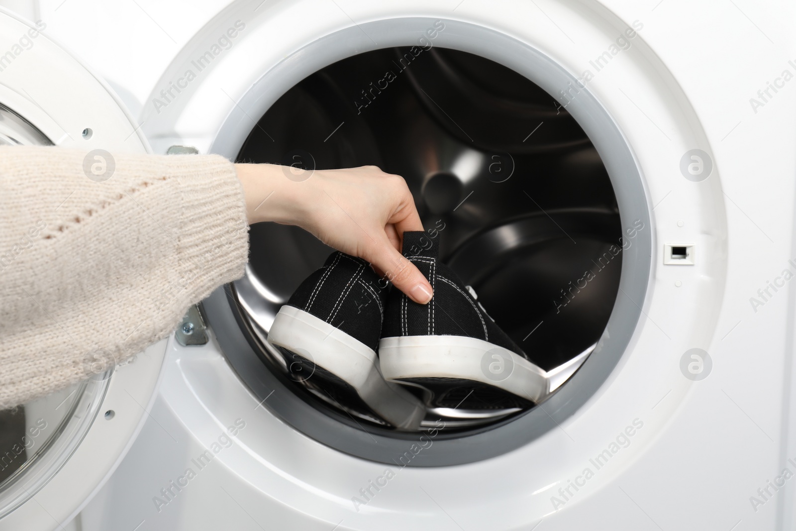 Photo of Woman putting stylish sneakers into washing machine, closeup